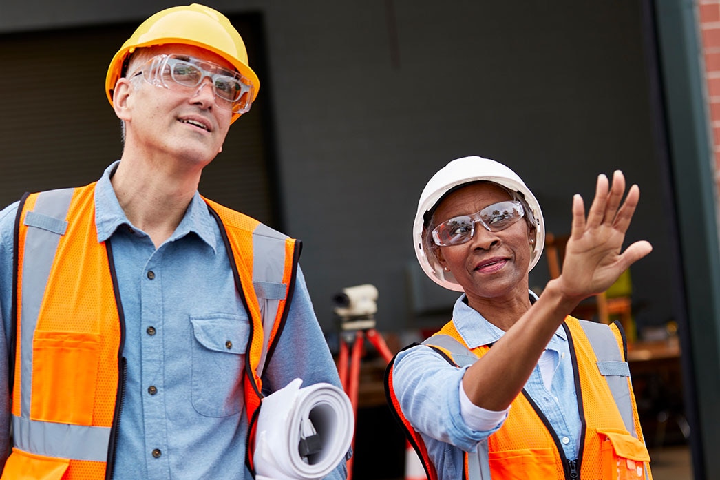 Workers carrying building plans discuss construction