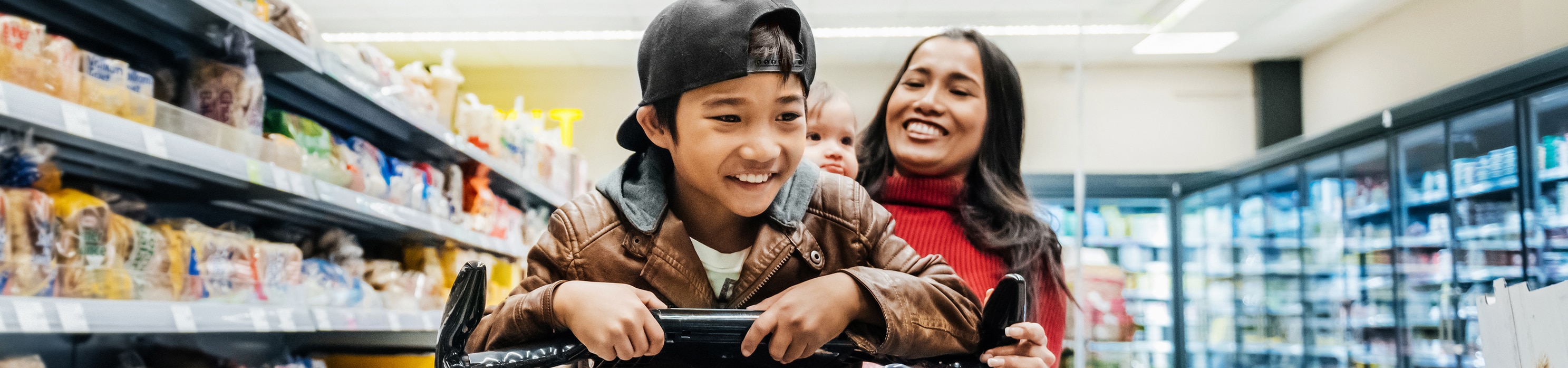 Smiling parent pushing their child on a shopping cart at a grocery store