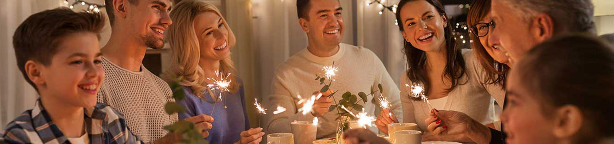 A smiling family sits together at the dinner table holding sparklers