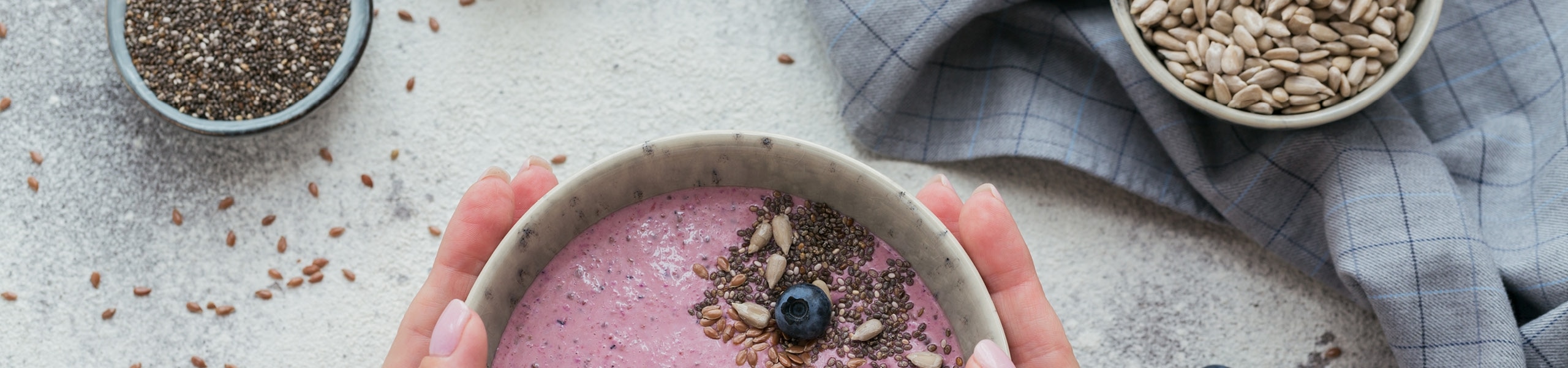 Person holding a bowl filled with a purple smoothie topped with seeds 