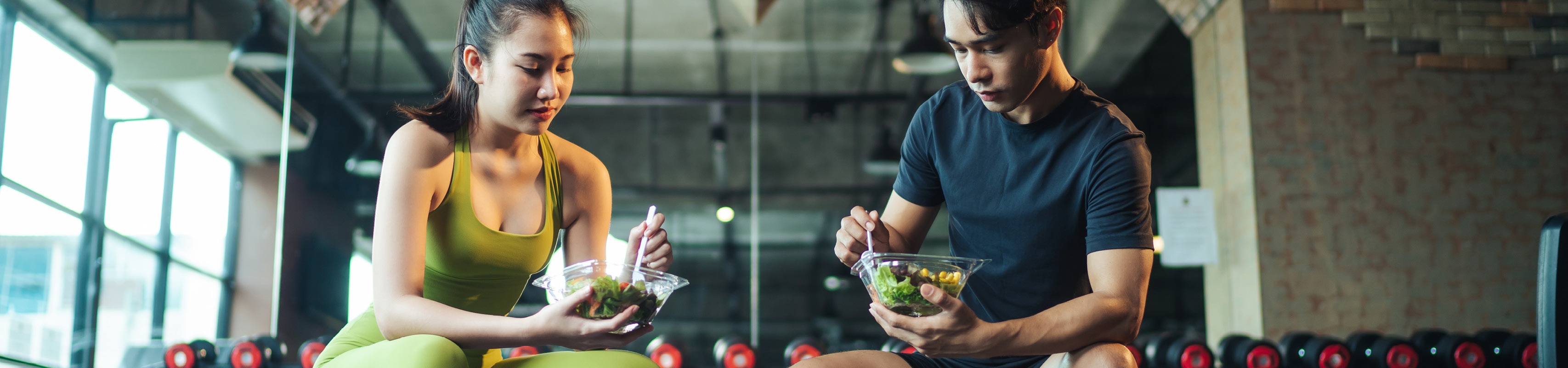 Two athletes eating small salads at the gym