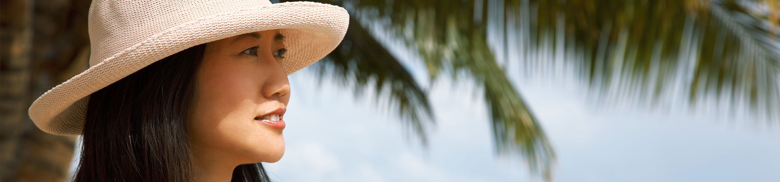 Person in a sun hat standing next to a palm tree