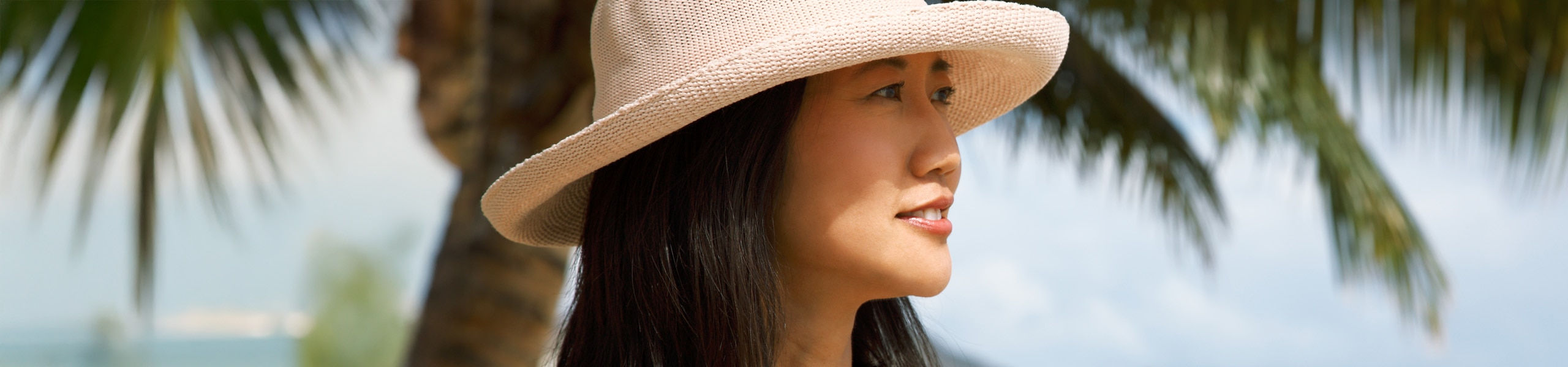 Person wearing a sun hat and standing by a palm tree