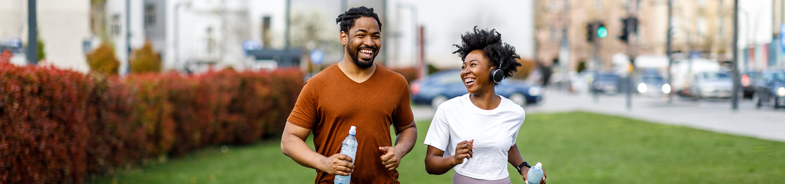 Smiling couple jogging in athletic clothes in a city park.