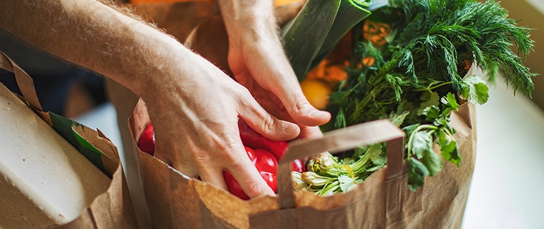 Hands reach into grocery bag containing vegetables