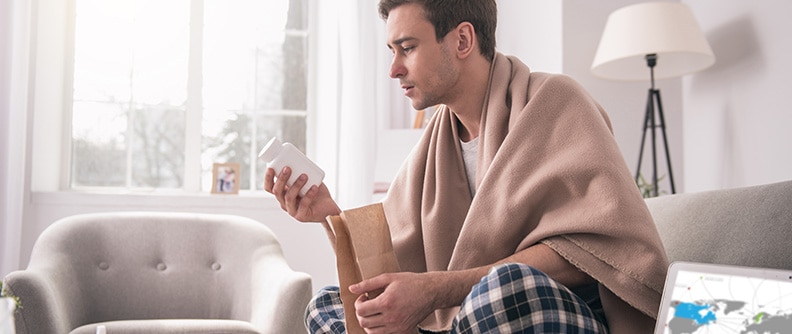 A man sits on a couch and reads medication bottle