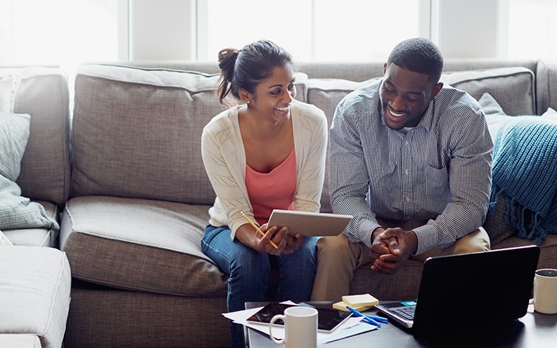 A smiling couple on a couch reviews papers