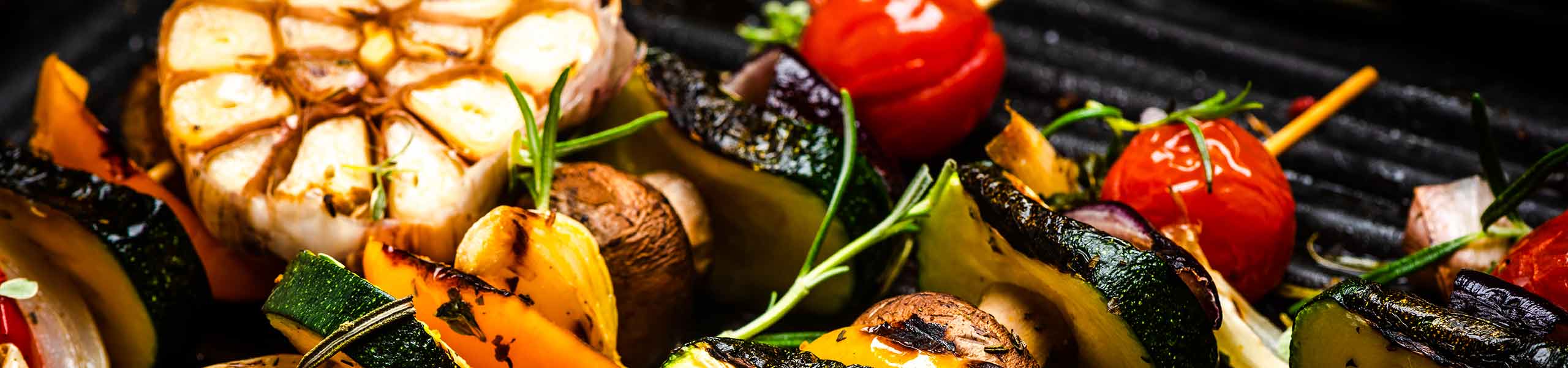 A flaming BBQ grill with skewers of fresh summer vegetables on top. 