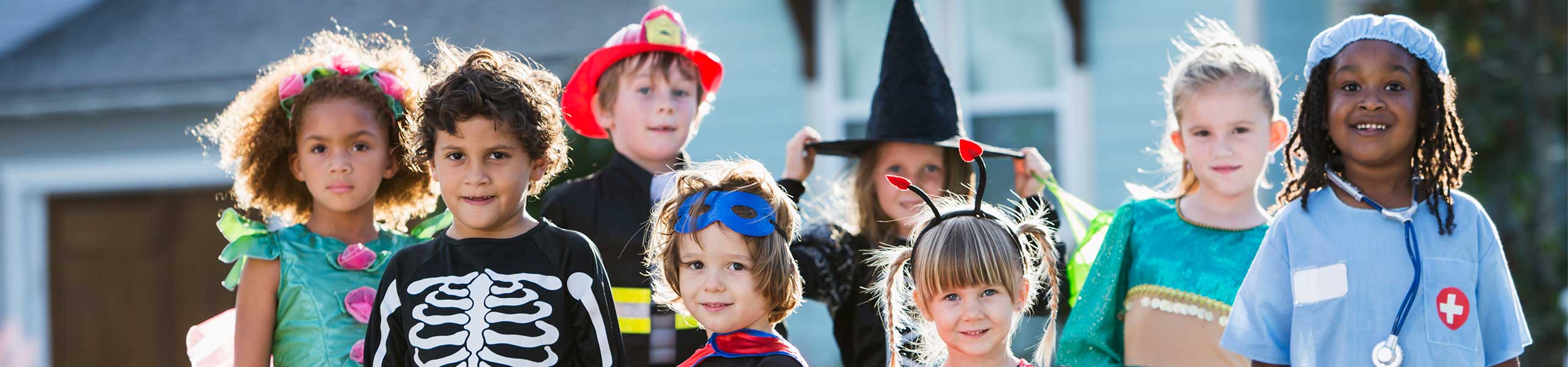 8 children of various ages standing outside wearing halloween costumes