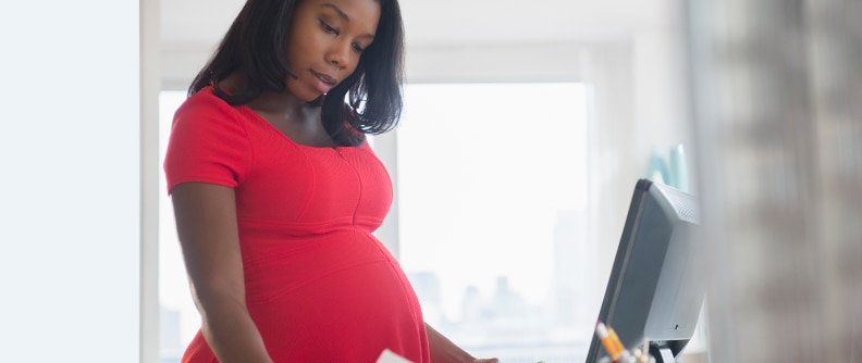 Pregnant person in red maternity shirt working in home office.