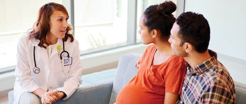 Pregnant couple consulting with doctor in waiting room.