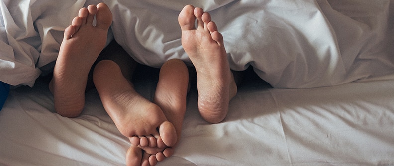 2 pairs of feet sticking out below bedsheets.