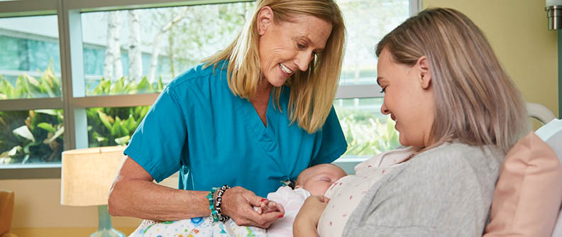 Nurse helping new mom breastfeed baby in hospital.