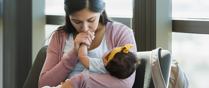 In doctor's waiting room, mother kisses baby's hand.