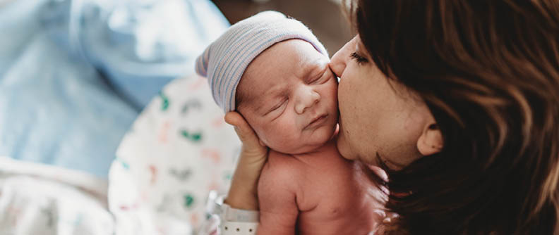 Close up detail of mother kissing newborn son's cheek in hospital.