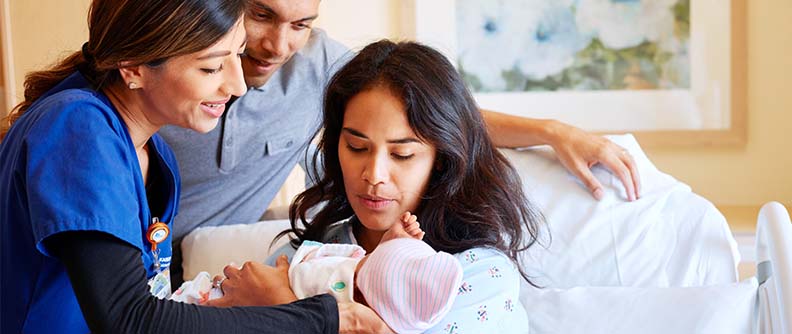 A new mother holds her baby in her arms while the father and doctor watch