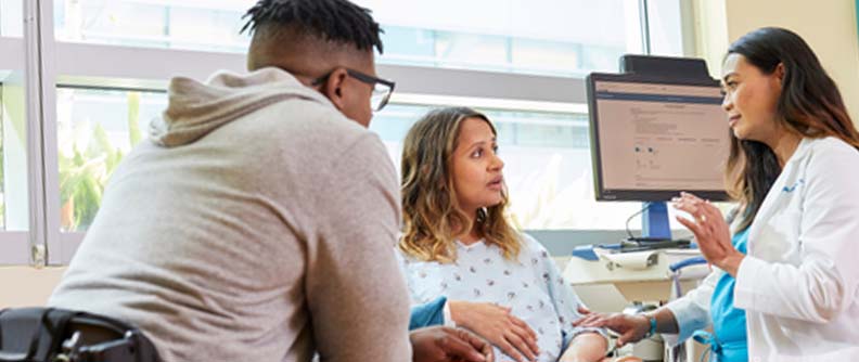 Doctor talking to pregnant person and partner at hospital.