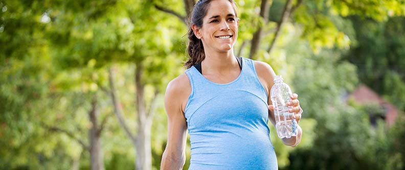 Pregnant woman walking and carrying a bottle of water.