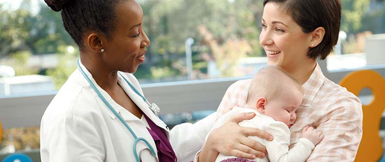 Parent holding baby and talking with doctor outside.