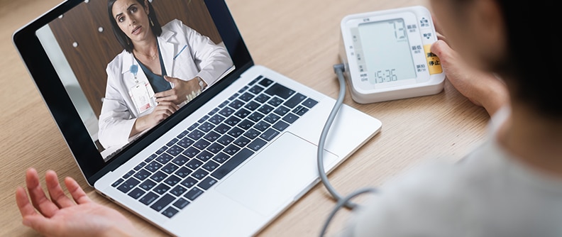 Woman checking blood pressure at home with virtual doctor on laptop