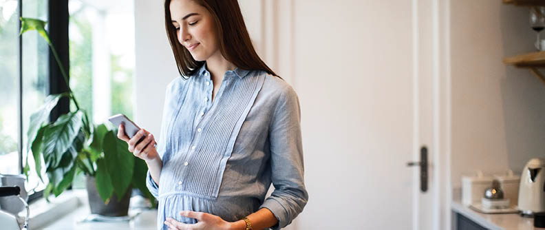 Young pregnant woman using mobile phone at kitchen counter.