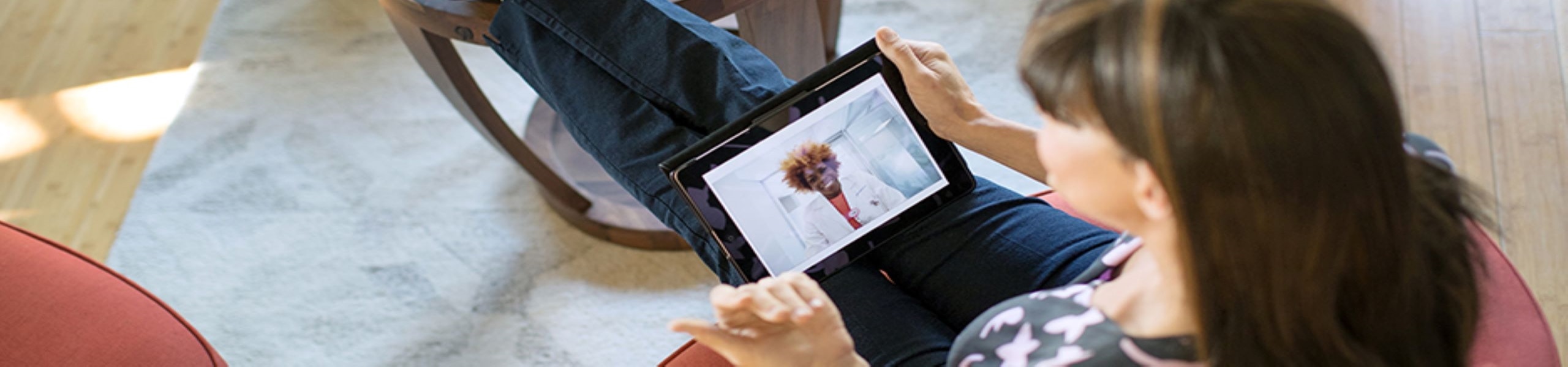Overhead shot of person sitting with their feet up, speaking with a clinician on a tablet