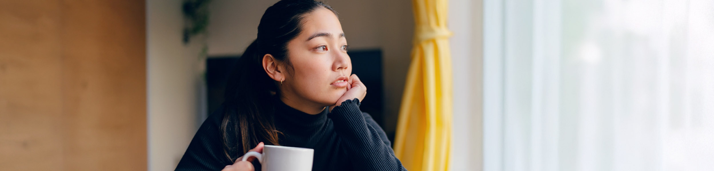 Young woman sitting by window enjoying a hot beverage