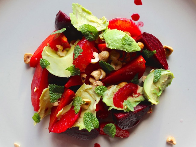 Salad of avocado, orange, beet, and hazelnut on a white plate.