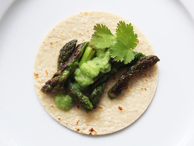 corn tortilla topped with asparagus pieces and green salsa and garnished with a sprig of cilantro