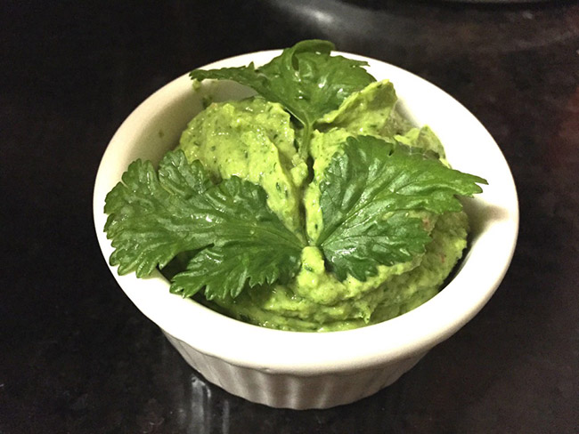 A bowl of 'brocamole' in a white ramekin, on a black countertop. 
