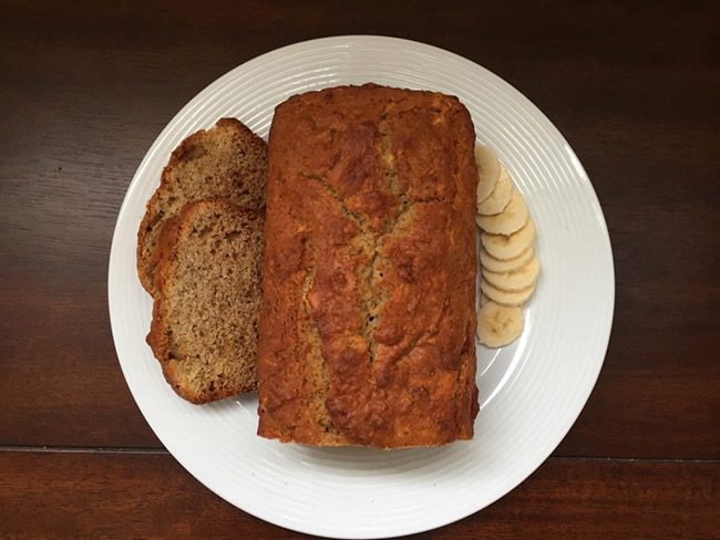 Sliced bown rice banana bread on a plate with sliced banana. 