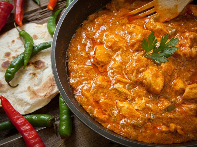 Chicken in a red sauce in a bowl on a table with peppers.