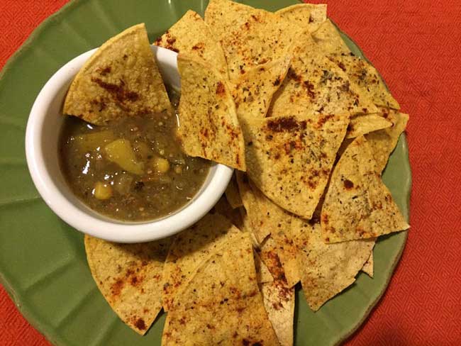A green plate with homemade tortilla chips and a bowl of salsa on top.