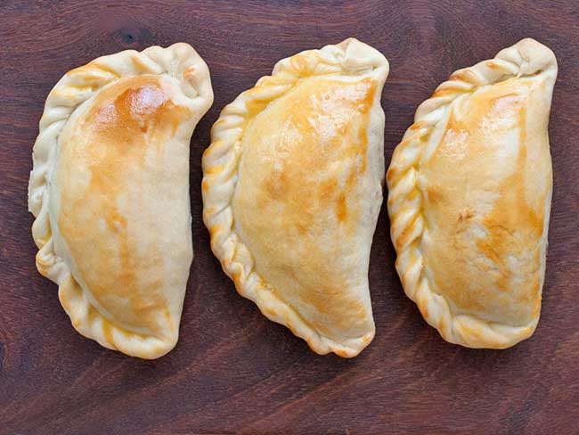 3 lightly toasted empanadas on a wooden tabletop.
