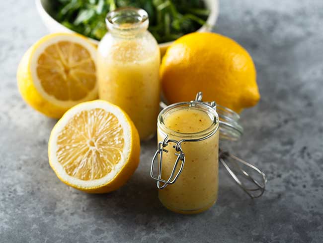 A mason jar filled with lemon vinaigrette with fresh lemons on the side.