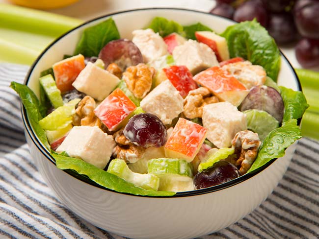 Chicken Waldorf salad served in a white ceramic bowl on a blue and white checkered tablecloth. 