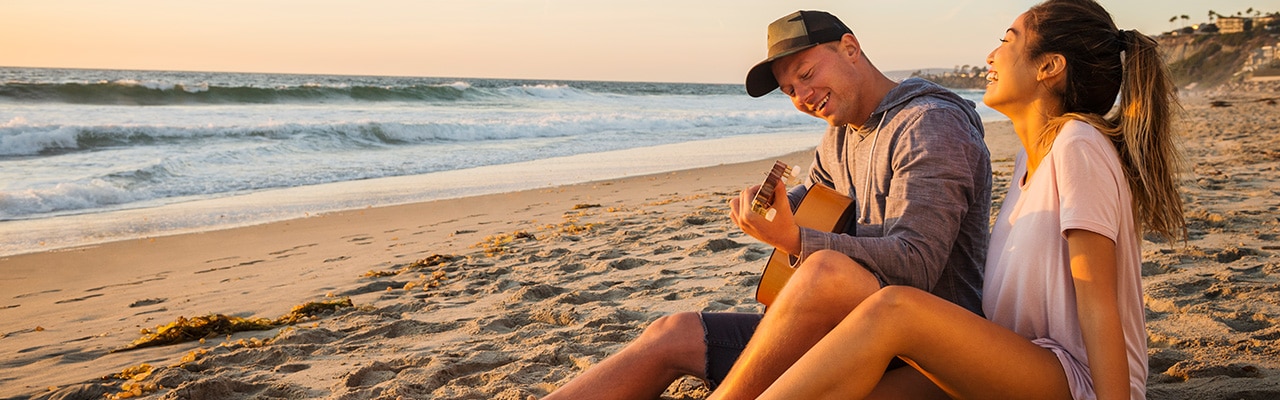 A happy couple plays guitar on the beach