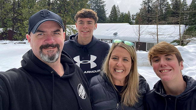 Mariann Stephens with her husband and 2 sons smiling, with snow and trees in the background. 