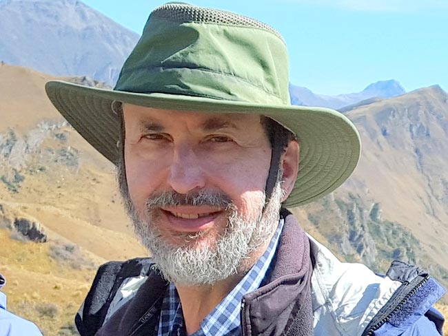 A man in a green brimmed hat hiking in the mountains.
