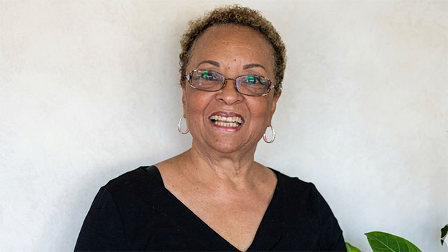 Person wearing a black shirt and glasses smiling against a white wall backdrop.