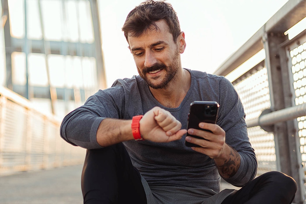 Person checking wearable device while holding mobile phone