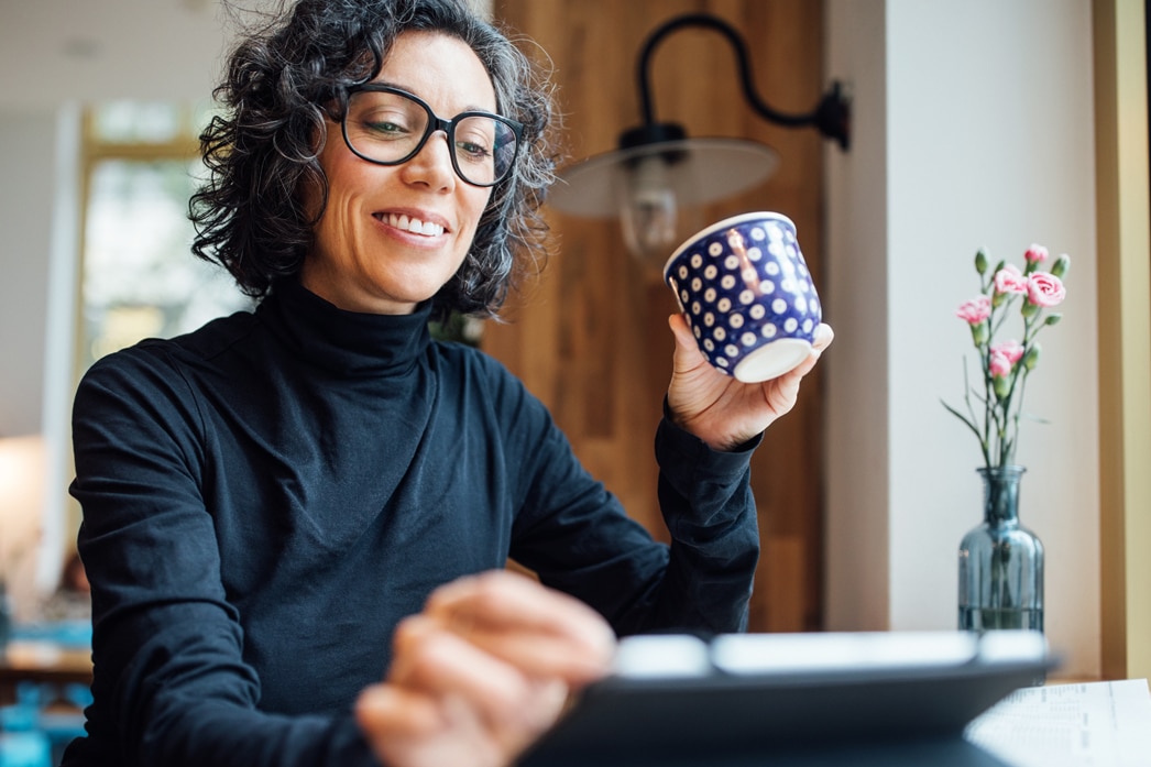 Person sipping coffee from a mug while reading tablet