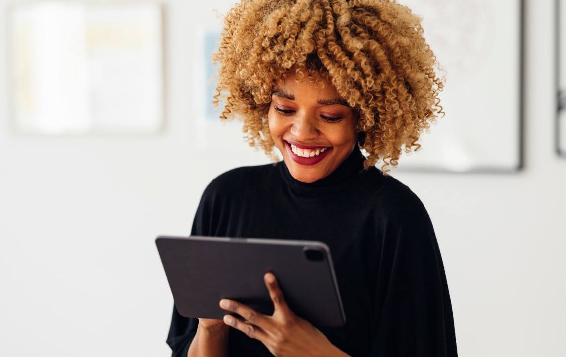 Happy businesswoman sitting on her desk using her tablet