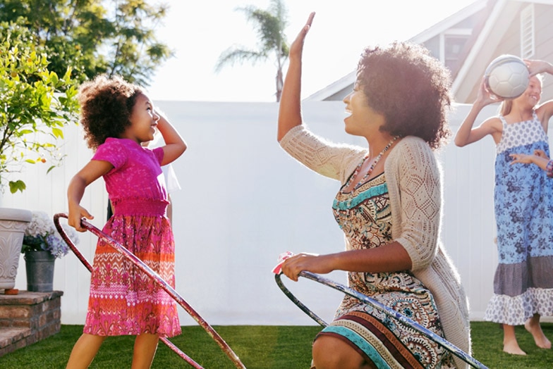 Parent and child playing with Hula-Hoops in backyard