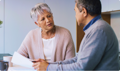 Two people sitting at a table indoors, reviewing papers during a conversation