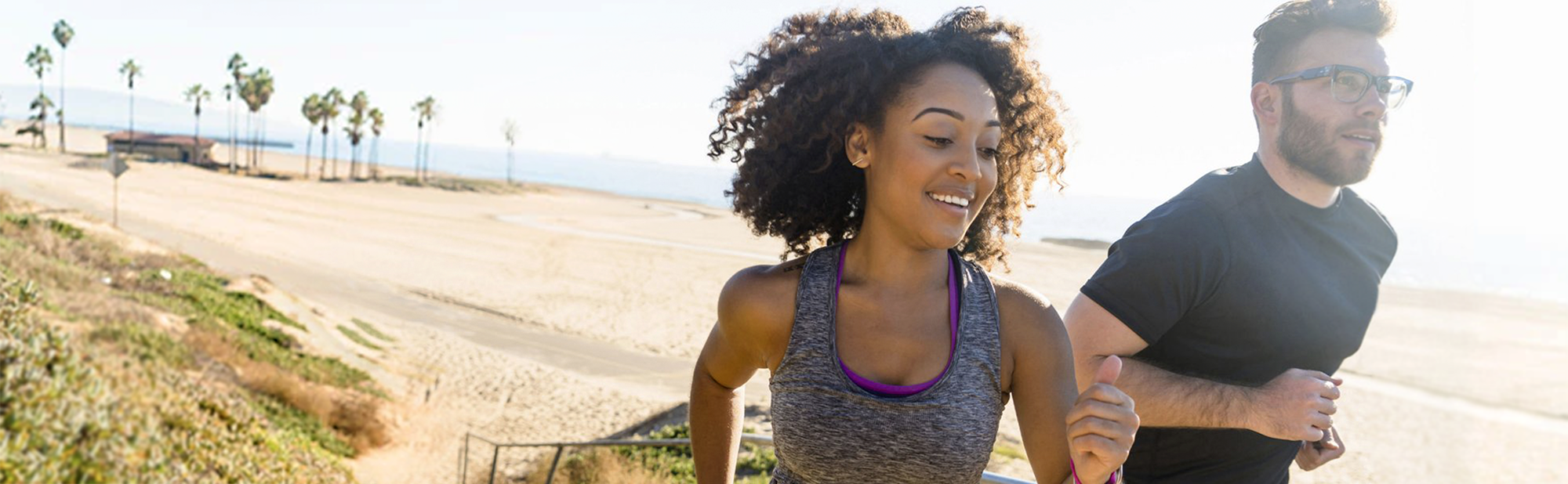 Young man and woman jog by beach