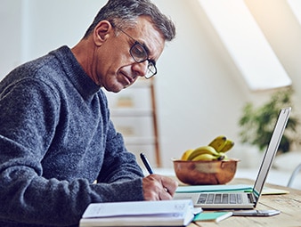 Man writes as he works at a laptop