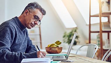 Man writes as he works at a laptop