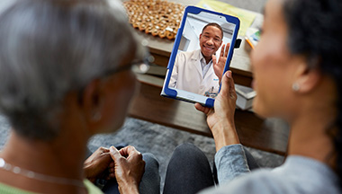 Two women look at a doctor on a tablet