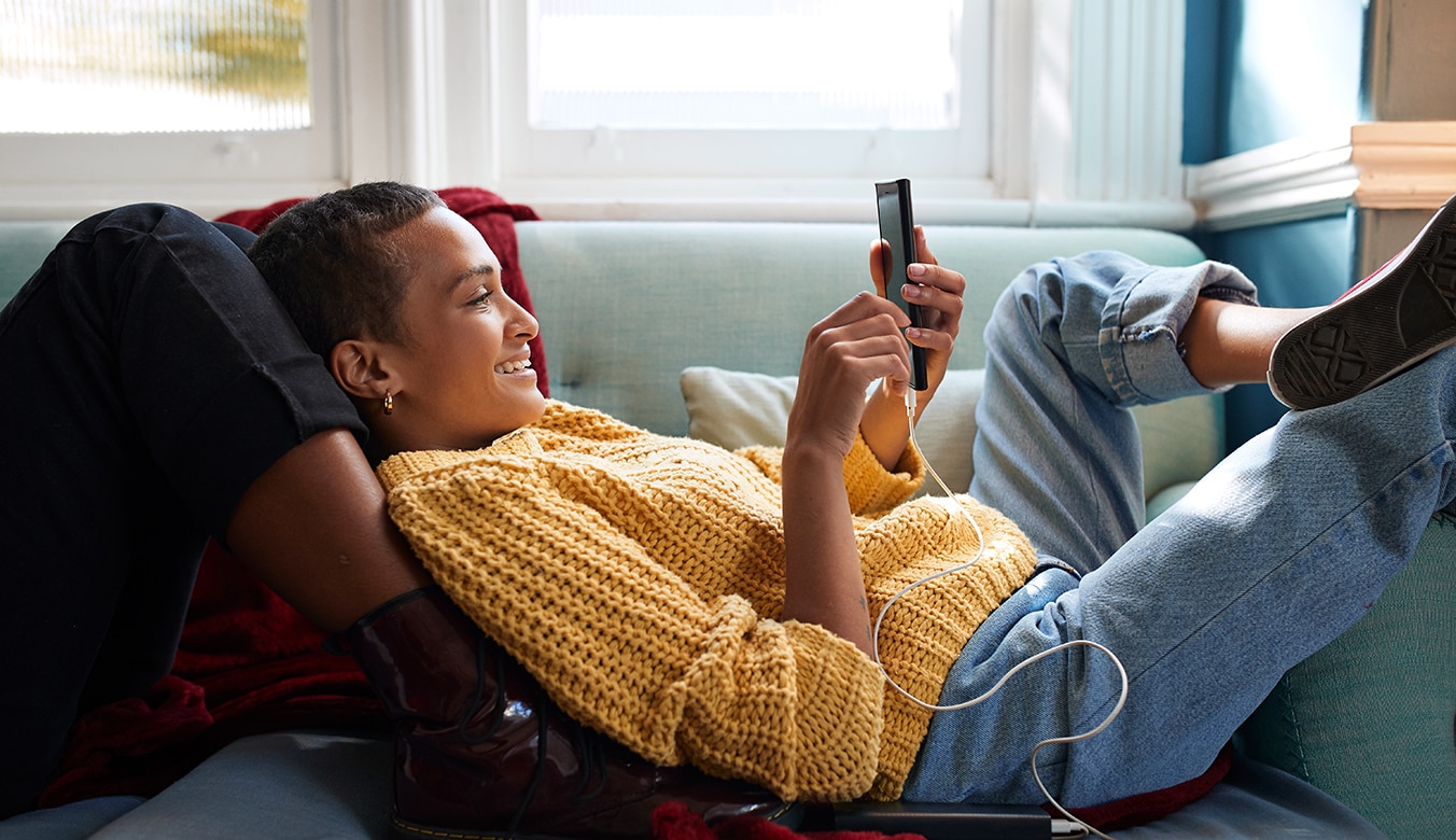 Person smiling at phone while lounging on couch